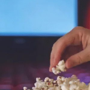 Person holding a tub of popcorn in a cinema hall with an empty audience and a blank screen in the background.