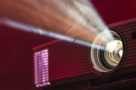 Projector beaming light onto a screen in a dark red cinema room.