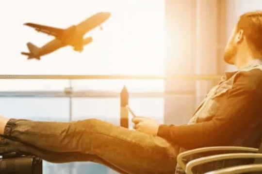 Man relaxing at an airport terminal while watching a plane take off during sunrise.