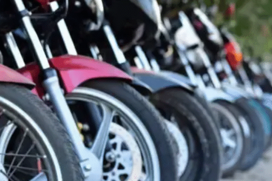 Row of parked motorcycles aligned on a street in daylight, focusing on the front wheels.