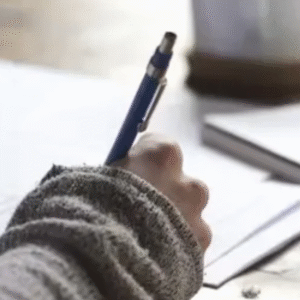 Student writing with a pen on paper during study or exam preparation.