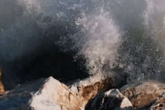 Powerful ocean waves crashing dramatically against rugged coastal rocks, creating a misty spray.