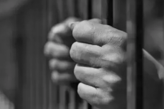 A pair of hands tightly gripping prison bars, symbolizing confinement or imprisonment.