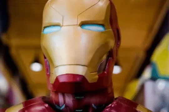 Close-up of an Iron Man suit replica with glowing blue eyes, captured indoors under warm lighting.