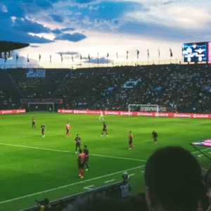 Professional football match underway in a packed stadium during sunset with players in action and crowd watching intensely.