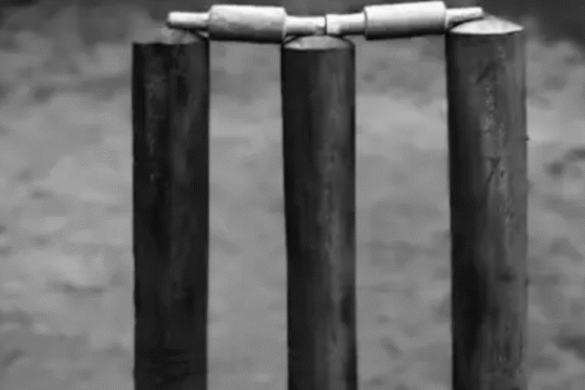 Close-up of cricket stumps and bails on a dusty pitch, captured in black and white.