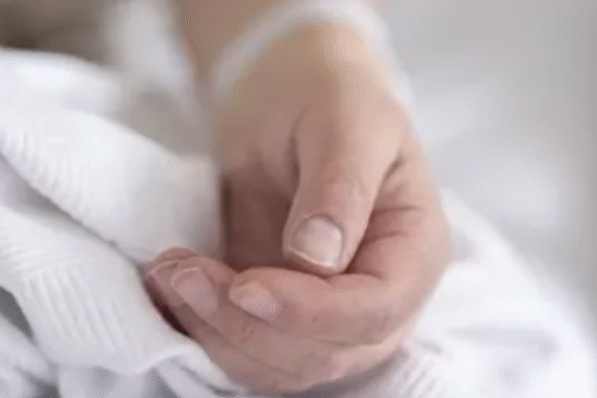 Close-up of a person’s hand resting on a white hospital blanket, symbolizing health emergency or critical condition