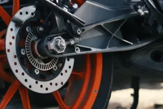 Close-up view of a motorcycle's rear wheel with orange alloy rims and disc brake system