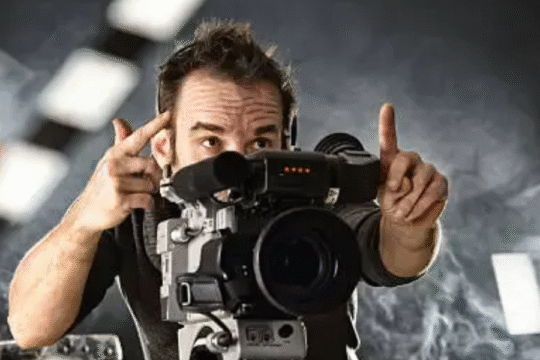 Film director framing a shot through a professional video camera with studio lights in the background