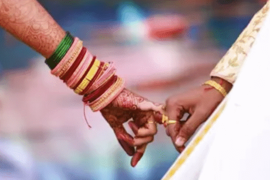Close-up of an Indian bride and groom holding hands during a traditional wedding ceremony, showcasing colorful bangles and henna designs.