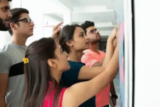 Group of Indian students checking exam results on a notice board with focused expressions.