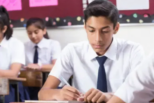 Group of Indian school students in uniform writing exams in a classroom setting.