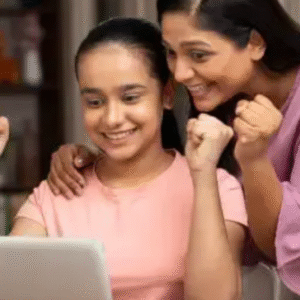 A happy teenage girl celebrating exam results on a laptop with her smiling mother beside her, showing excitement and pride at home.