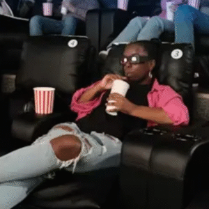 People relaxing in a modern movie theater, wearing 3D glasses and enjoying drinks and popcorn in recliner seats.
