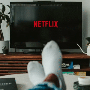 Person relaxing at home while watching Netflix on a TV screen, surrounded by indoor plants and a guitar in the background.