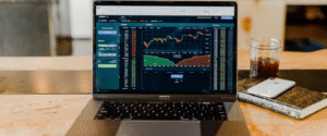 Laptop displaying stock market charts, next to a phone and a drink.