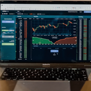 Laptop displaying stock market charts, next to a phone and a drink.