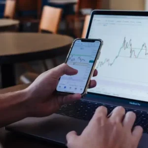 A person reviews financial charts on both a smartphone and a laptop.