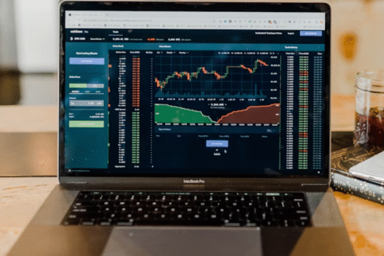 Laptop displaying stock market charts, next to a phone and a drink.