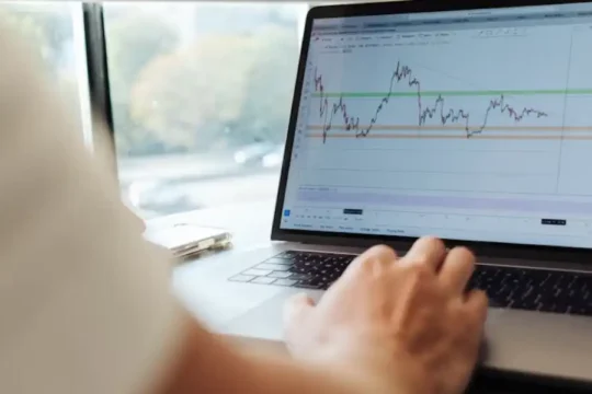 A person's hands are on a laptop keyboard, displaying a financial chart on the screen.