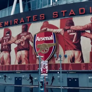 Emirates Stadium exterior with a large mural of Arsenal football legends.