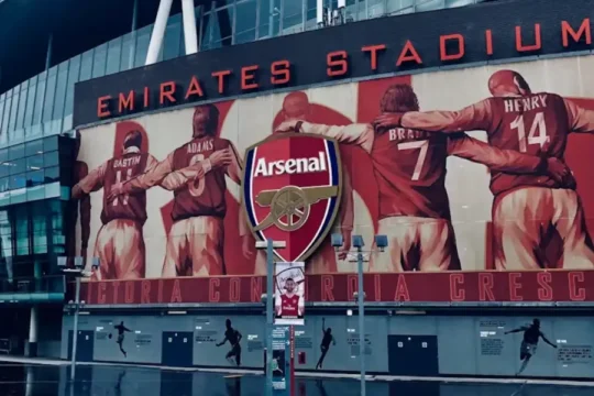 Emirates Stadium exterior with a large mural of Arsenal football legends.