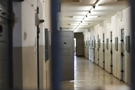 View through cell bars of a long, narrow prison corridor.