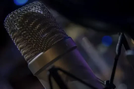 A professional condenser microphone with a blurred background of lights.