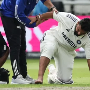 Cricketer on knees, receiving assistance from two support staff.