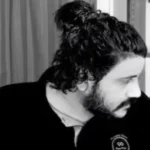 Man with long hair tied in a bun, looking down in black and white.