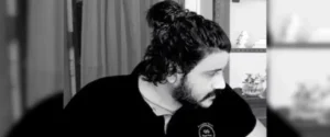Man with long hair tied in a bun, looking down in black and white.