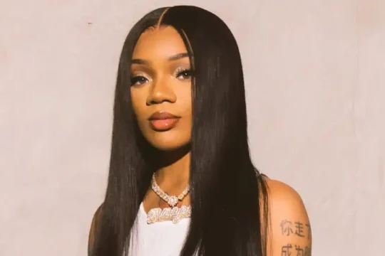 Suki Waterhouse in a white top, looking directly at the camera.