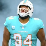 Football player Christian Wilkins in Miami Dolphins uniform, emerging from smoke.