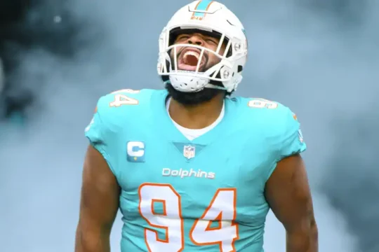 Football player Christian Wilkins in Miami Dolphins uniform, emerging from smoke.