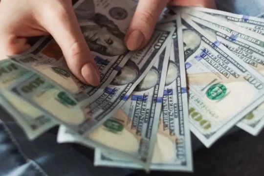 Hands fanning out a stack of one hundred dollar bills.