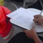 A student with long dark hair takes notes on a tablet arm desk.