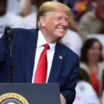 Donald Trump smiling and leaning on a podium with the Presidential Seal.