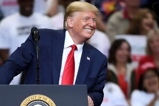 Donald Trump smiling and leaning on a podium with the Presidential Seal.