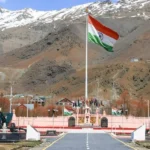The Indian flag flies high at a war memorial in a mountainous region.