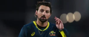 An Australian cricketer in uniform with a beard, looking thoughtfully.