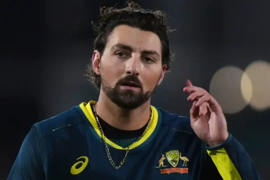 An Australian cricketer in uniform with a beard, looking thoughtfully.