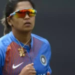 An Indian female cricketer in blue jersey and sunglasses, looking focused.