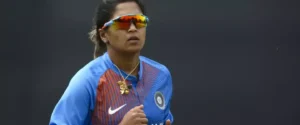 An Indian female cricketer in blue jersey and sunglasses, looking focused.