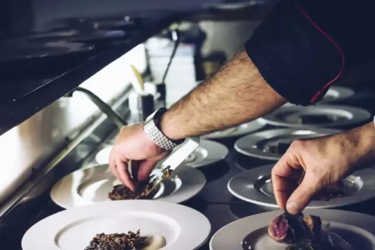 A chef's hands carefully plating dishes in a dark kitchen environment.