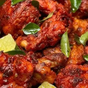 A plate of vibrant red fried chicken, garnished with lime wedges and green leaves.
