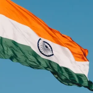 A large Indian flag (Tiranga) flapping in the wind against a clear blue sky.