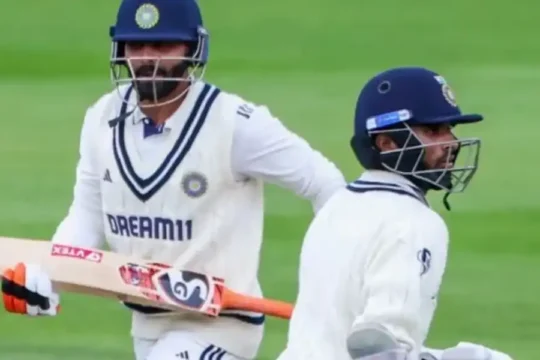 Two cricketers in white uniforms running between wickets on a green field