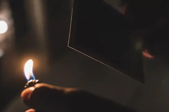 A hand holding a lit lighter in a dark room, illuminating a square object.