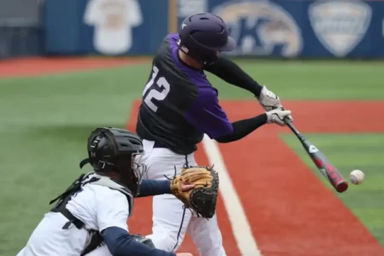 A baseball batter in a purple jersey hitting a ball, with a catcher and umpire behind him.