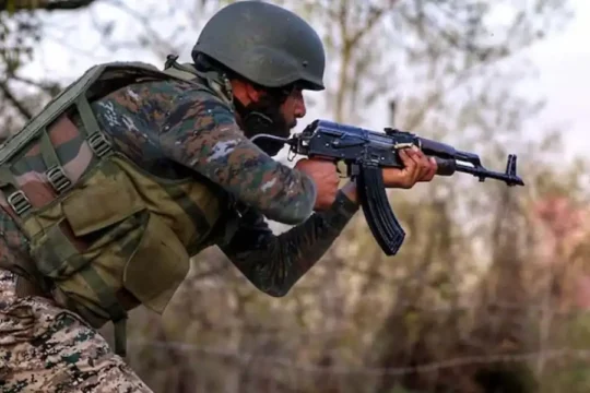 An Indian Army soldier in camouflage and helmet, aiming a rifle